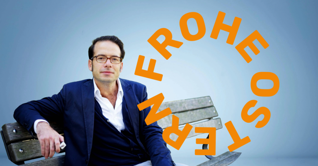 Oliver Rabbat, Cannabis-Anwalt aus Berlin, sitzt entspannt auf einer Parkbank vor blauem Hintergrund mit dem Schriftzug „Frohe Ostern“